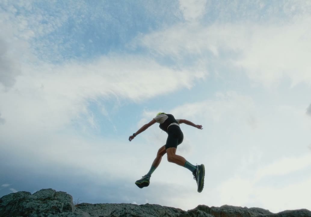 Trail runner jumping off a rock ridge